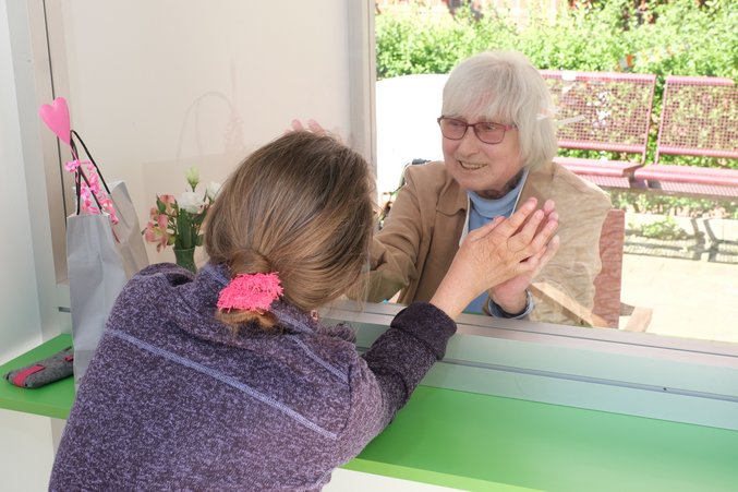 In der Klön-Bude sitzen eine ältere und eine jüngere Frau. Sie reden miteinander und legen ihre Hände aneinander.